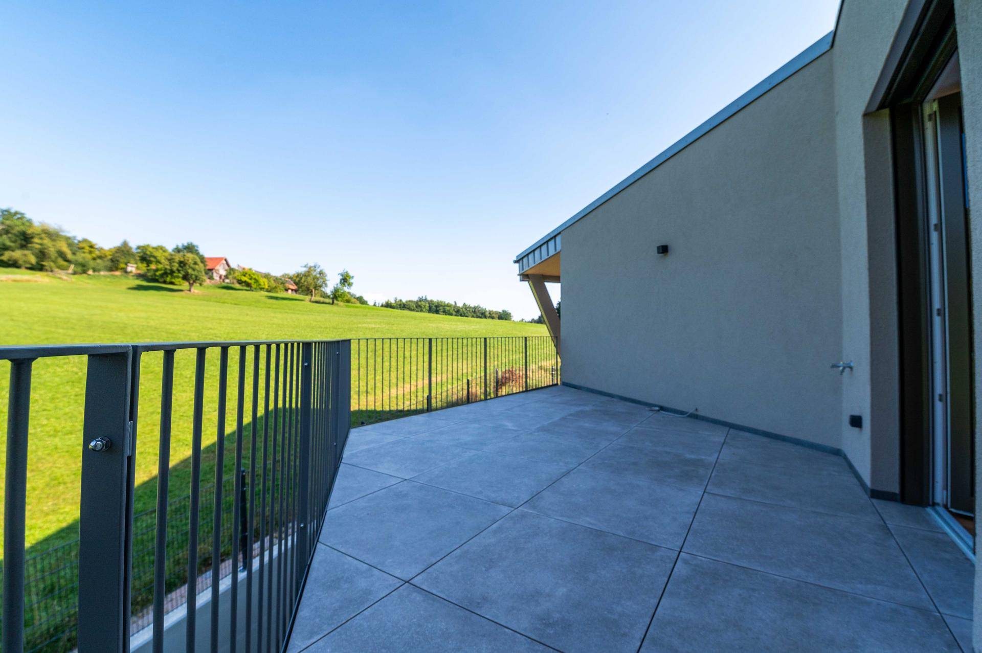 Große, geflieste Terrasse mit Metallgeländer und weitem Blick ins Grüne.