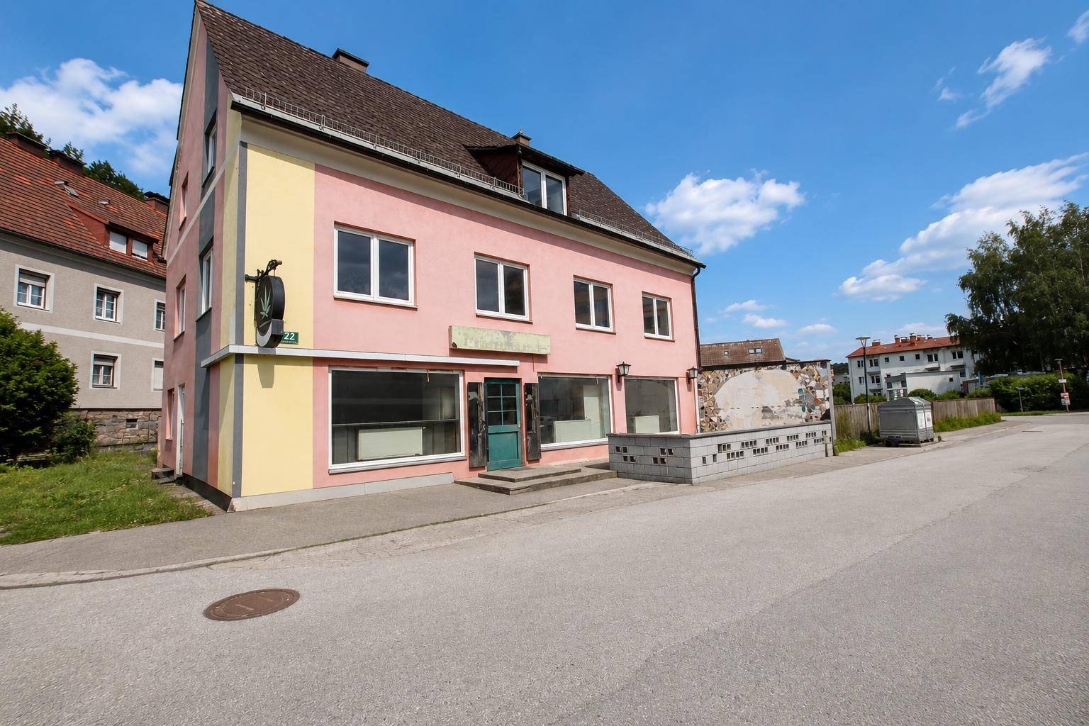 Nahaufnahme der rosa und gelben Fassade des Mehrfamilienhauses mit Schaufenstern im Erdgeschoss und Eingangstür.