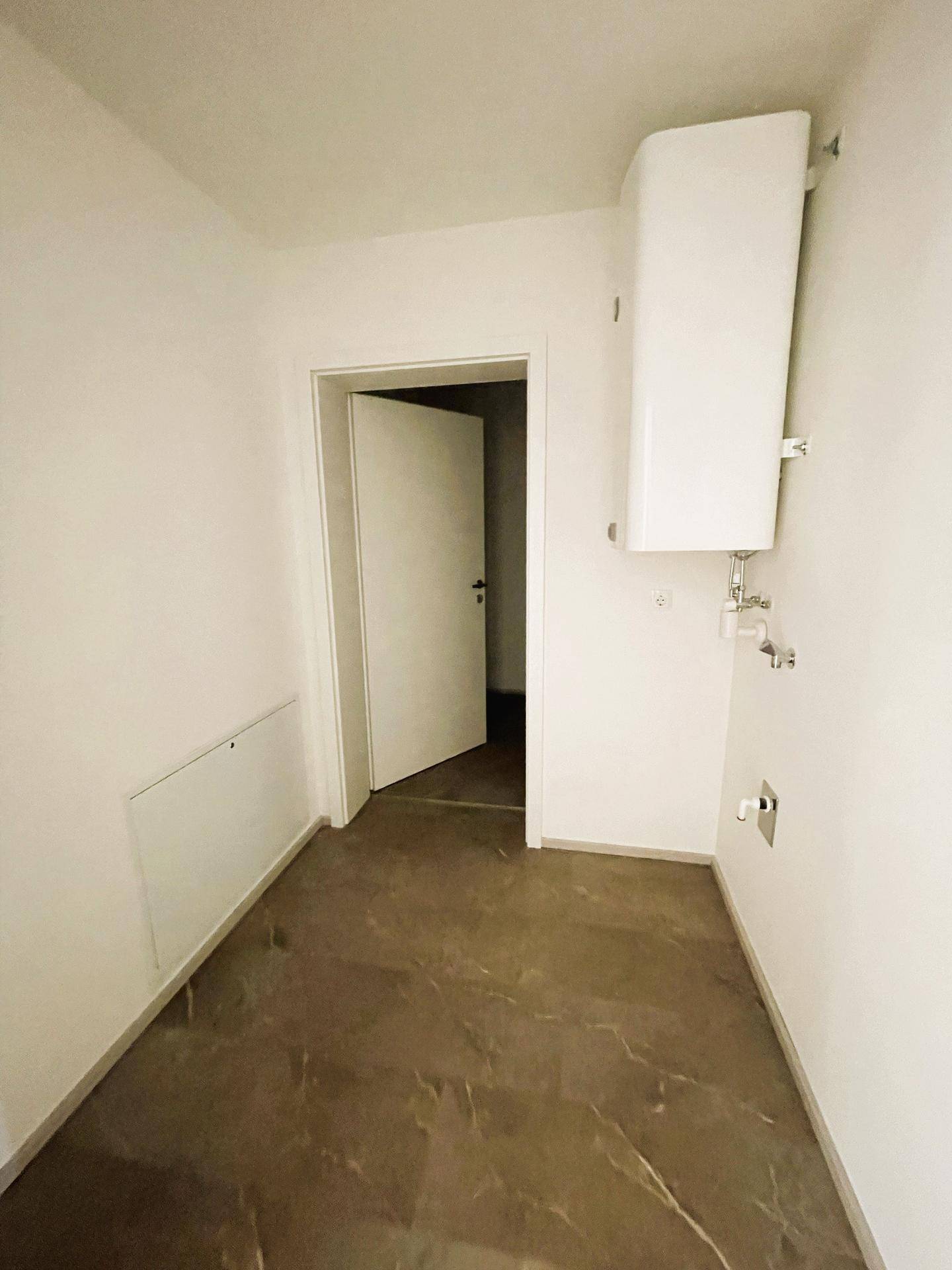 Praktischer Hauswirtschaftsraum mit dunklen Fliesen und einem Warmwasserbereiter an der Wand.