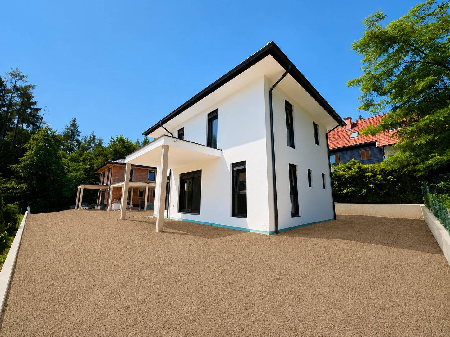 Weitläufige Außenansicht des Hauses mit Carport und Kiesfläche, umgeben von viel Grün.