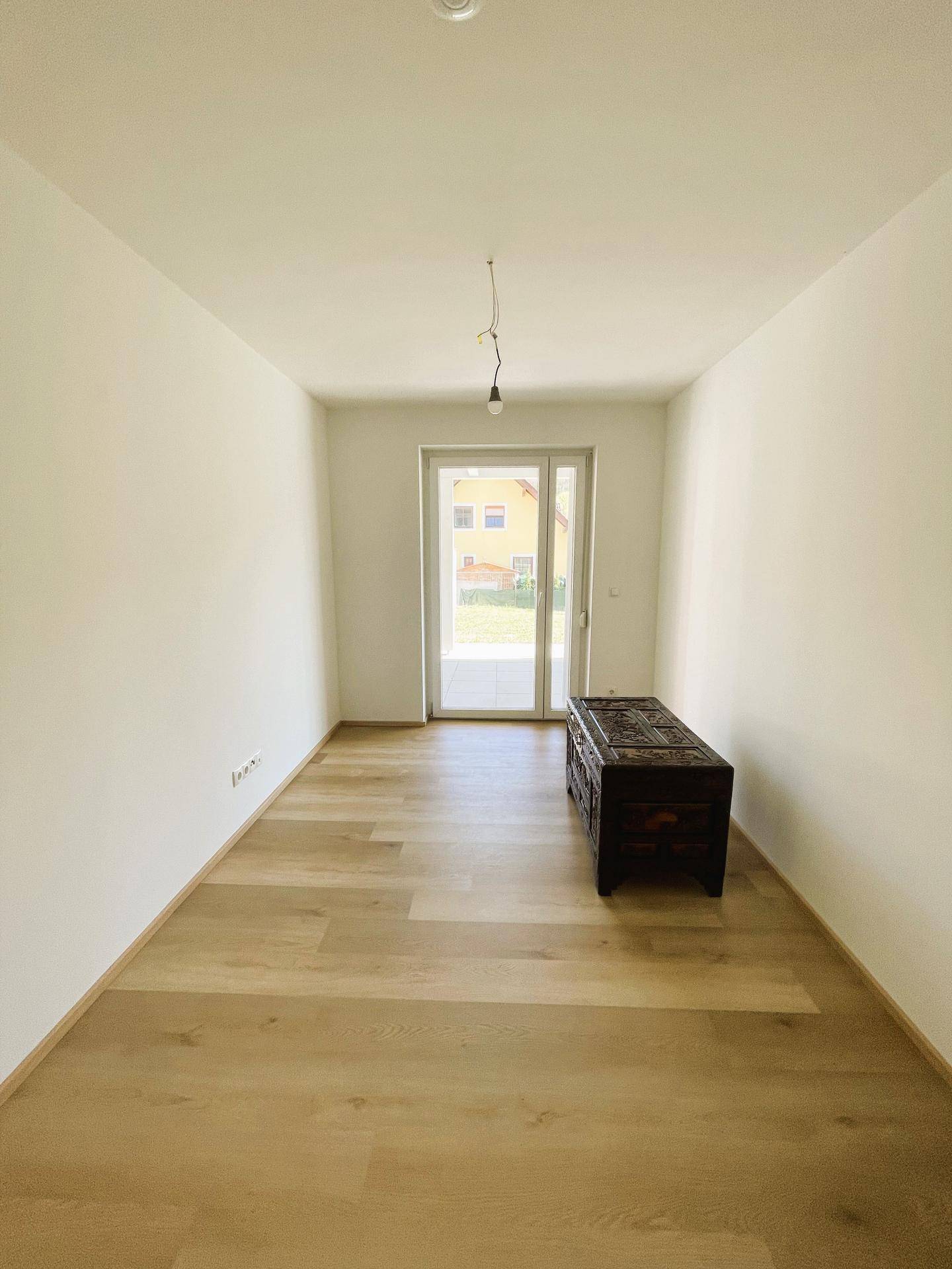 Helles Zimmer mit Parkettboden und Zugang zu einem privaten Gartenbereich.
