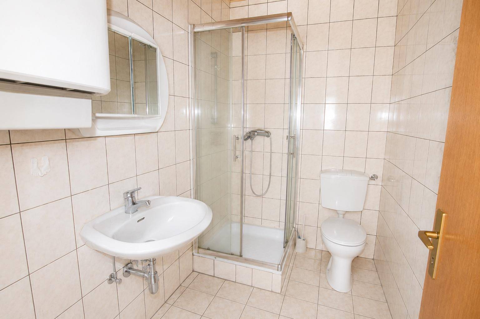 Kleines Badezimmer mit beigefarbenen Fliesen, Waschbecken, Toilette und Duschkabine.