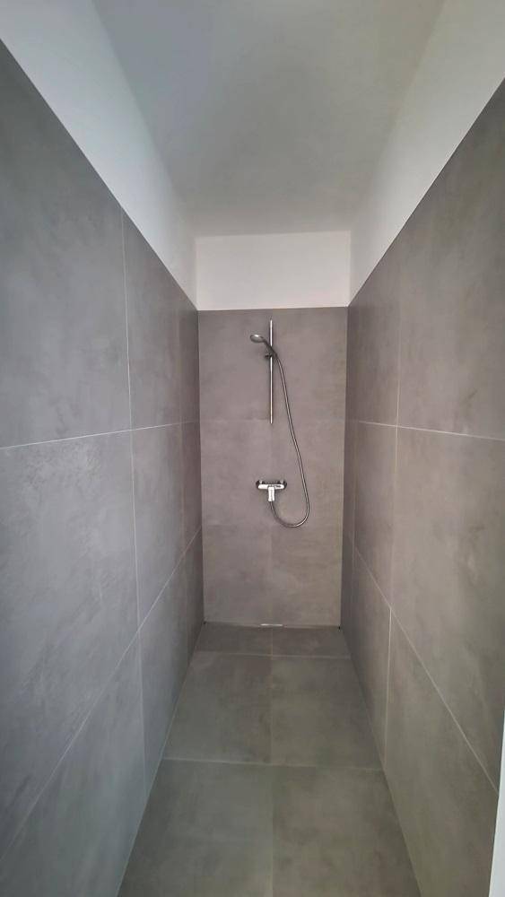 Geräumige begehbare Dusche mit modernen grauen Fliesen und einfacher Armatur.