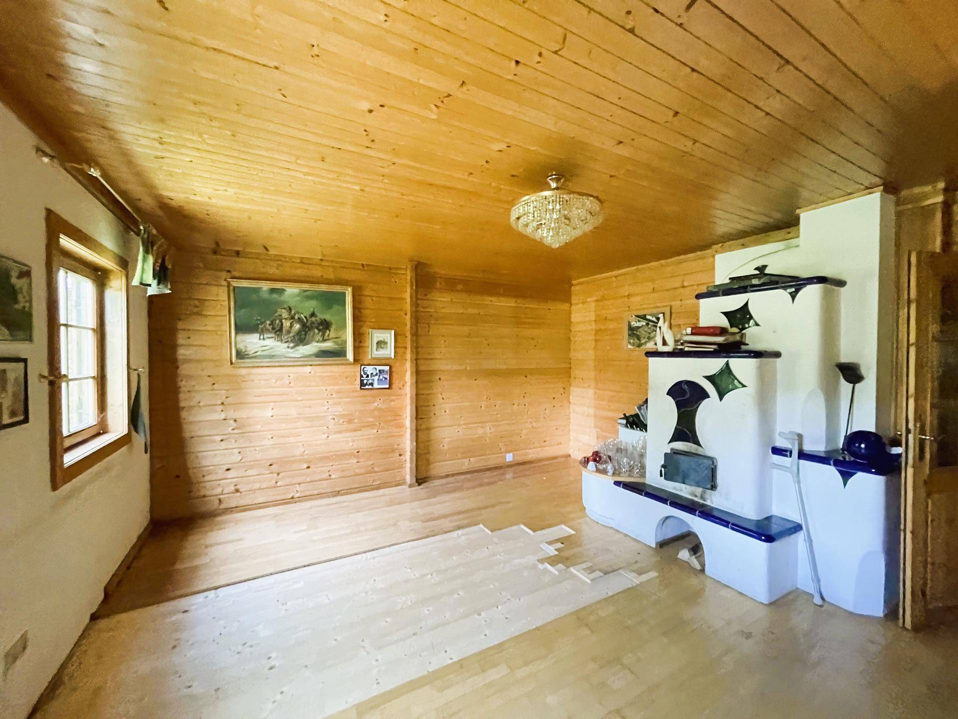 Gemütliches Wohnzimmer mit Holzwänden, Holzdecke und einem traditionellen Kachelofen.