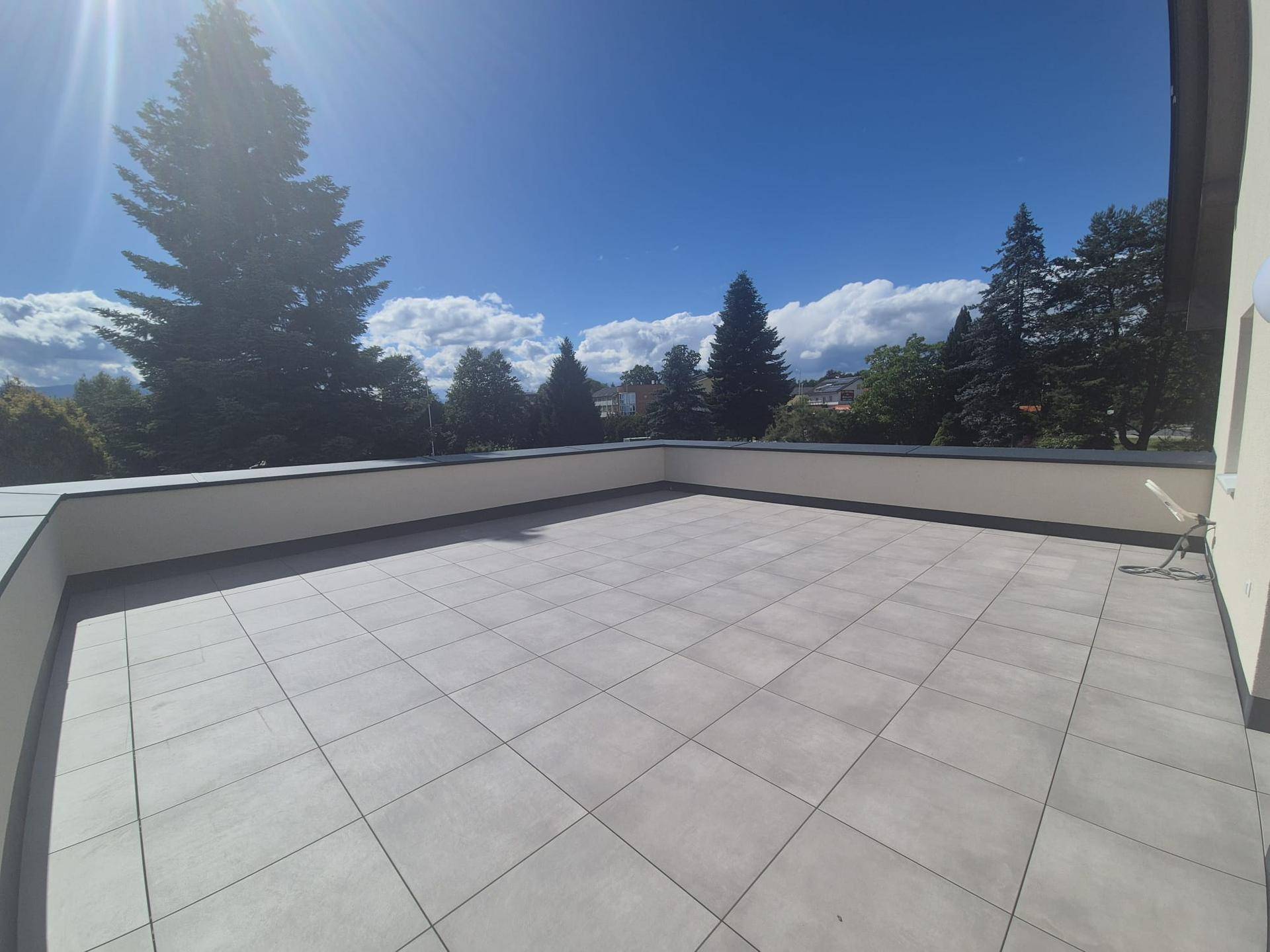 Weitläufige Dachterrasse mit hellen Fliesen und einem schönen Ausblick auf die grüne Umgebung.