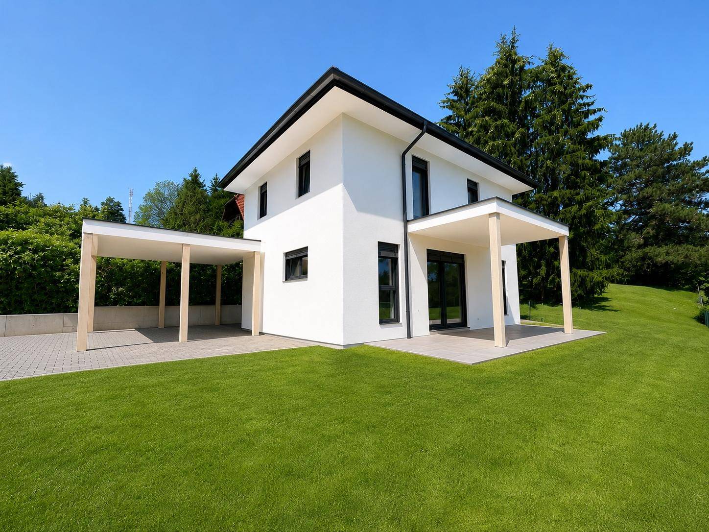 Modernes Einfamilienhaus mit weißer Fassade, Carport und gepflegtem Rasen unter blauem Himmel.