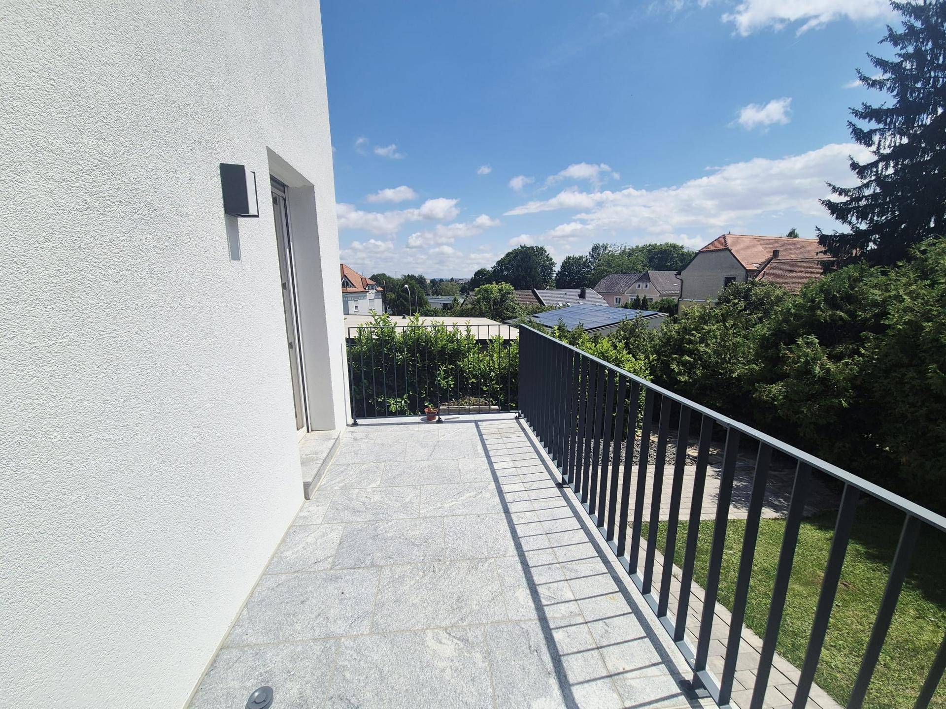 Sonniger Balkon mit Fliesenboden und weitem Blick über die grüne Landschaft und Häuser.