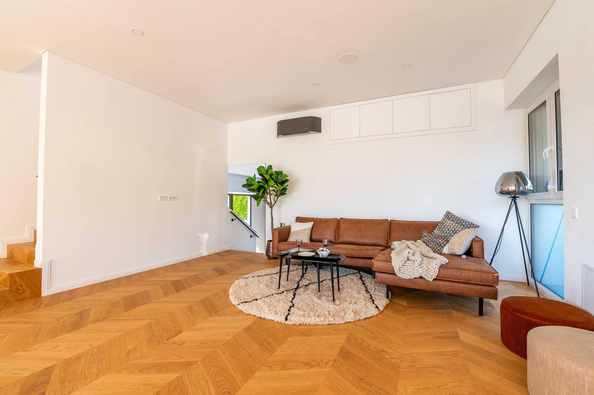 Heller Wohnbereich mit bequemer Ledercouch, Fischgrätparkett und Klimaanlage.