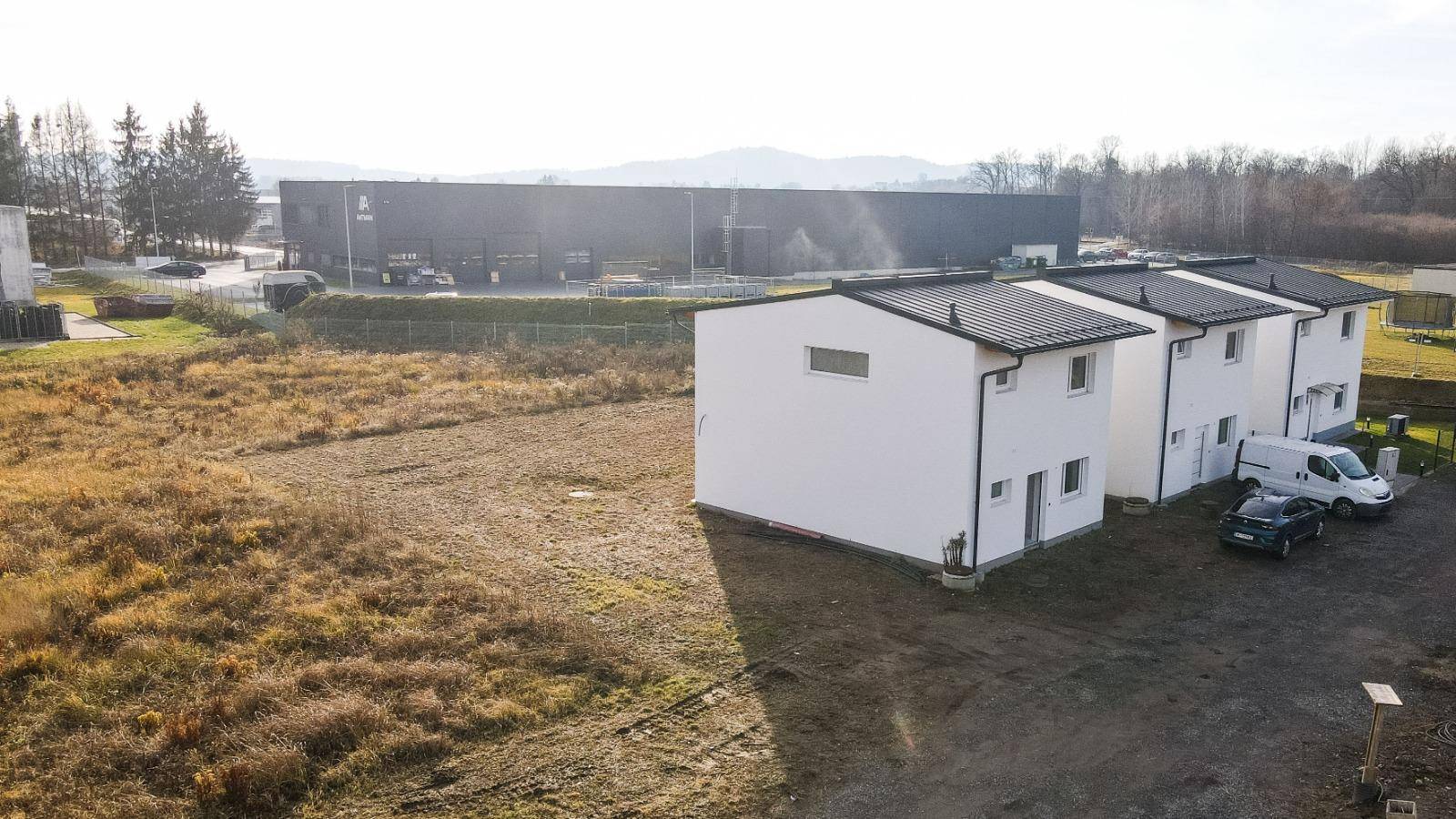 Luftaufnahme von drei neuen Häusern mit weißer Fassade und einem Industriegebäude im Hintergrund.