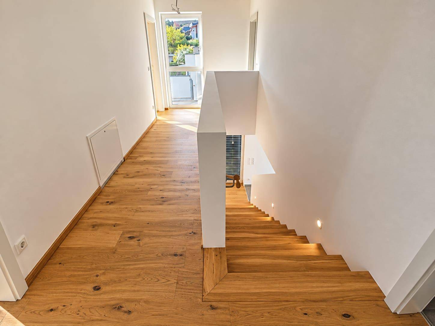 Heller Flur im Obergeschoss mit warmem Holzdielenboden und einer eleganten Holztreppe, die nach unten führt.
