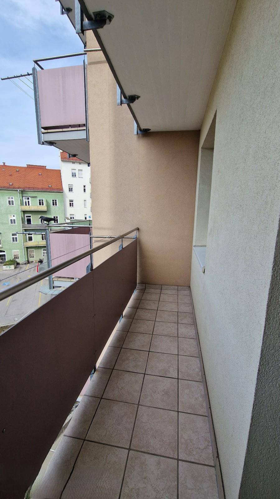 Schmaler Balkon mit Fliesenboden und Metallgeländer, bietet einen Blick auf die Umgebung.