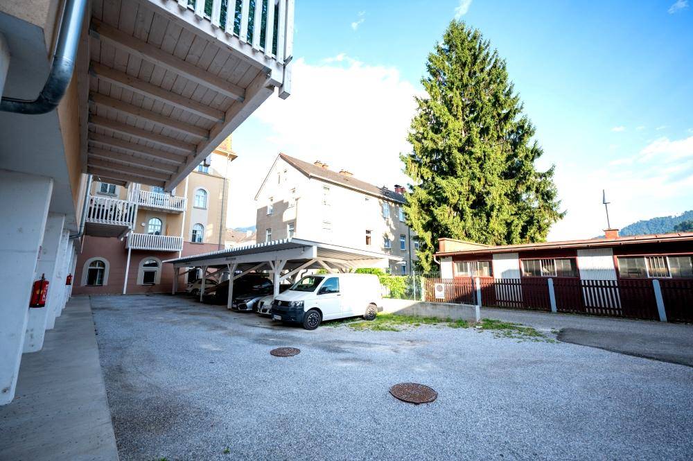 Überdachte Parkplätze und ein großer Baum neben einem Wohngebäude.