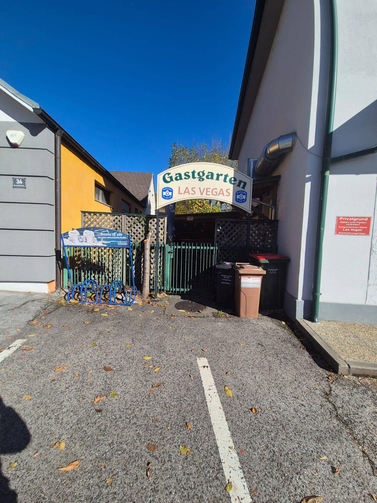 Eingangsbereich zum Gastgarten mit Fahrradständern und Mülltonnen an einem sonnigen Tag.