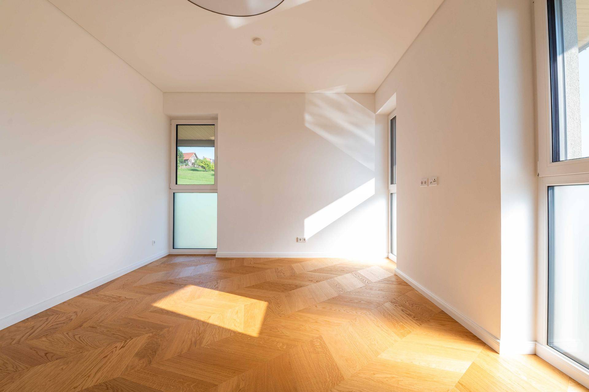 Helles Schlafzimmer mit Fischgrätparkett und sonnigen Lichtstrahlen auf dem Boden.