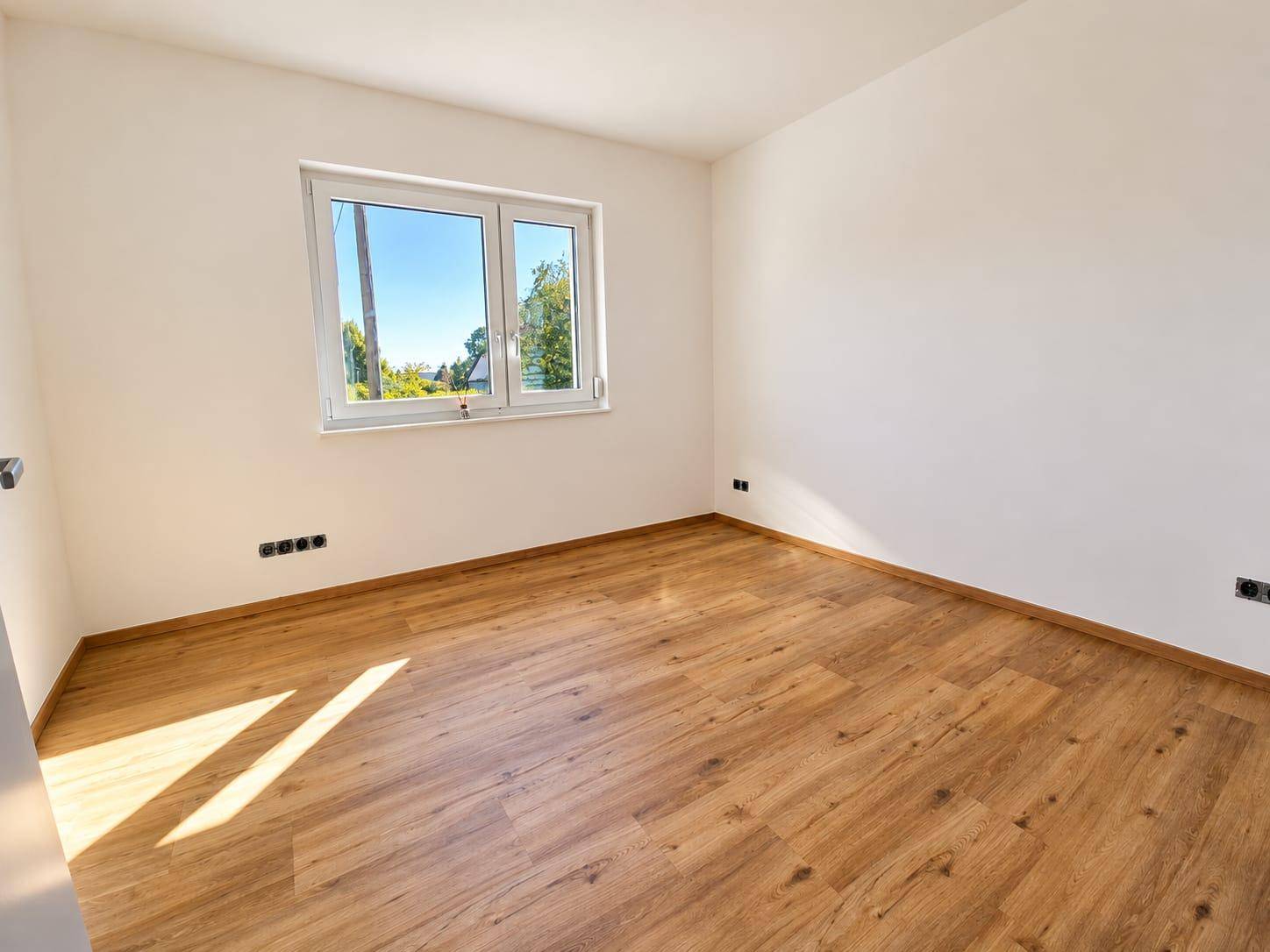 Geräumiges Zimmer mit hellem Laminatboden und Ausblick ins Grüne, ideal als Schlaf- oder Arbeitszimmer.