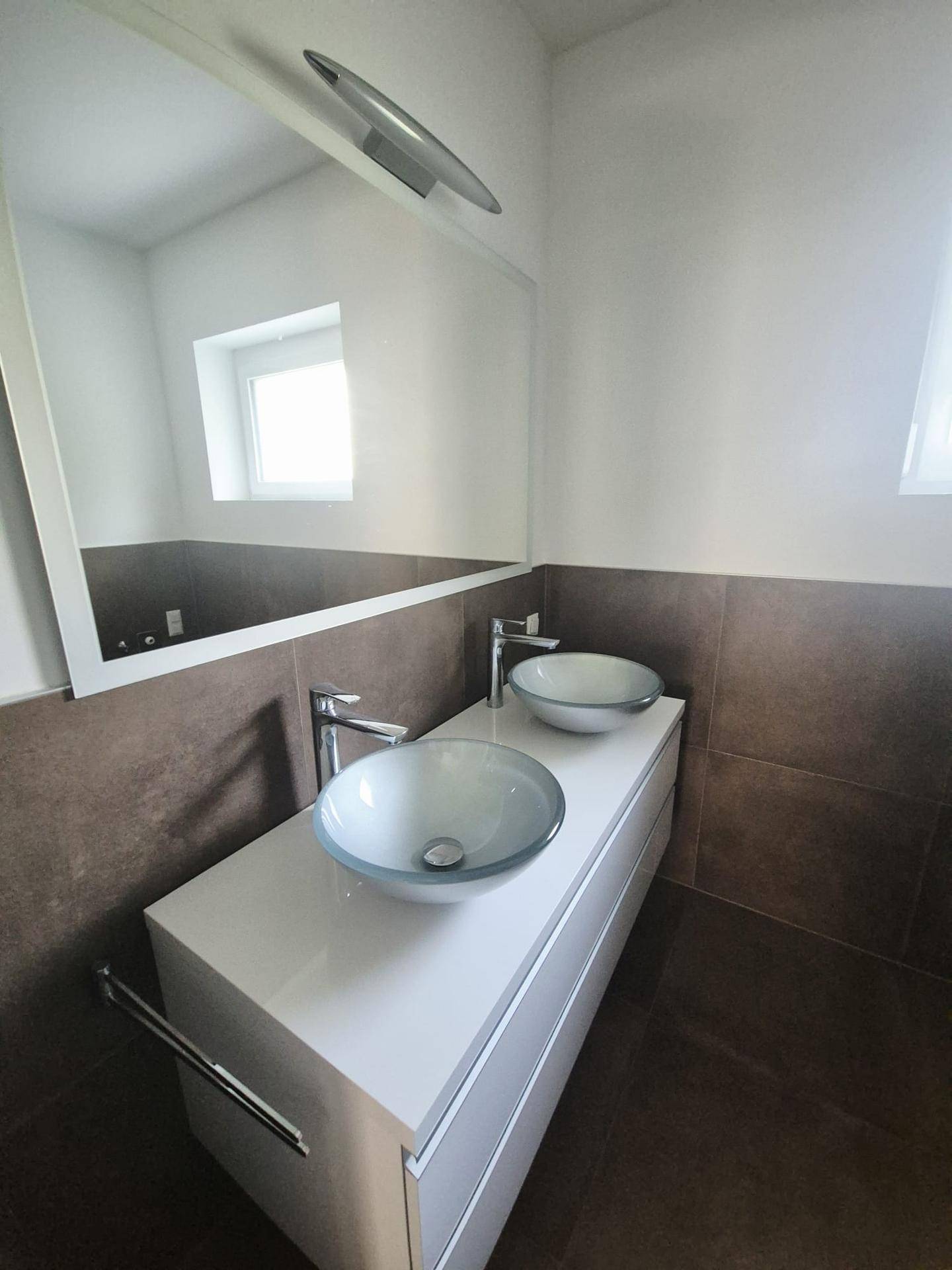 Modernes Badezimmer mit Doppelwaschbecken, großem Spiegel und braunen Fliesen.