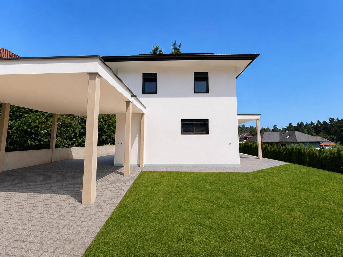 Seitenansicht des modernen Einfamilienhauses mit Carport und gepflastertem Bereich neben dem Rasen.
