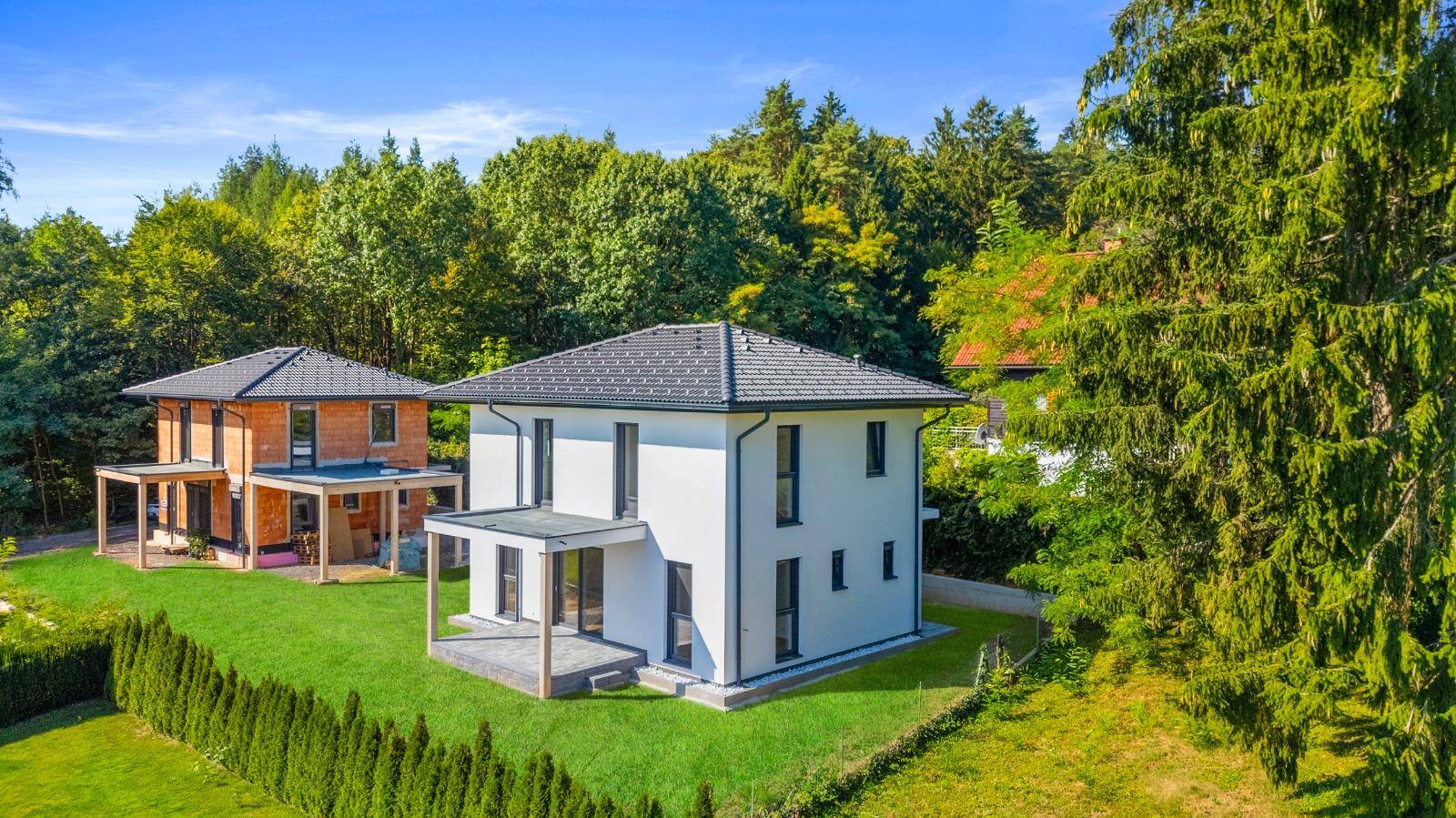 Zwei moderne Einfamilienhäuser mit gepflegtem Rasen und umgebendem Wald.