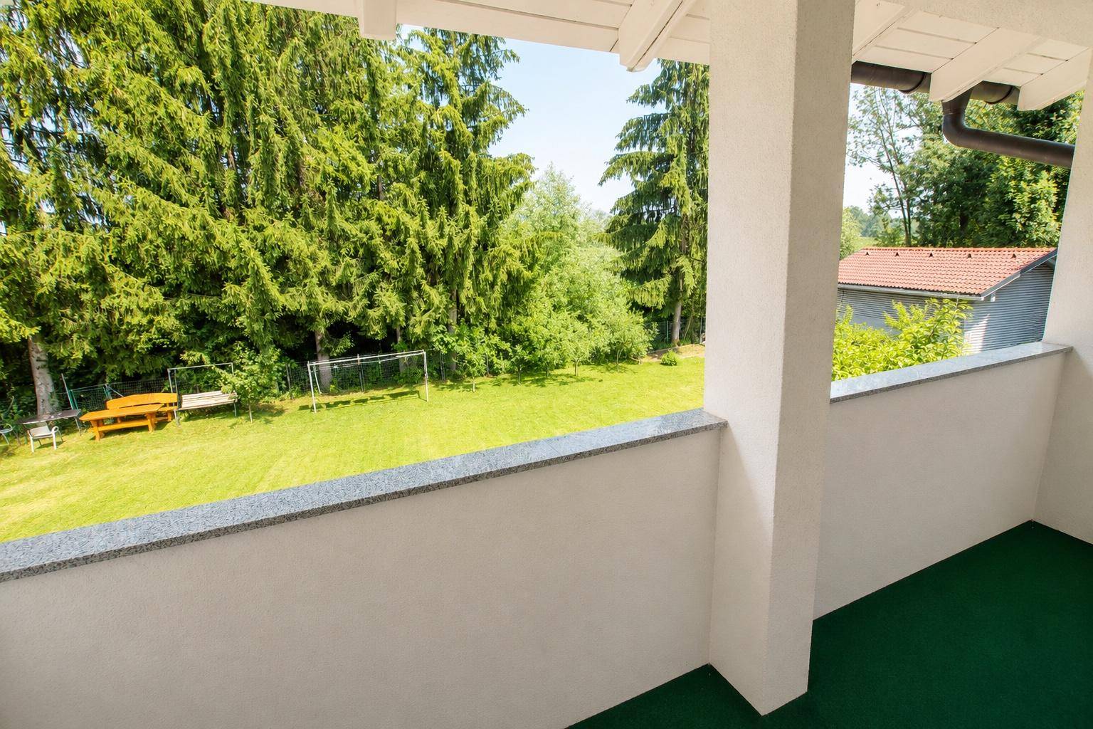 Balkon mit grünem Bodenbelag und weitem Blick auf den großen Rasen und die Bäume.