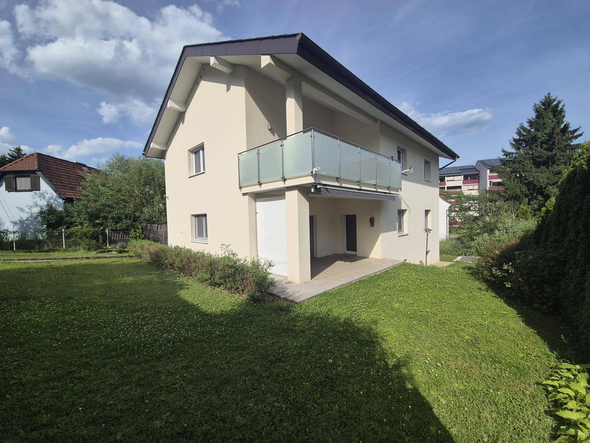 Gepflegtes Zweifamilienhaus mit Balkon und großzügiger Rasenfläche unter blauem Himmel.