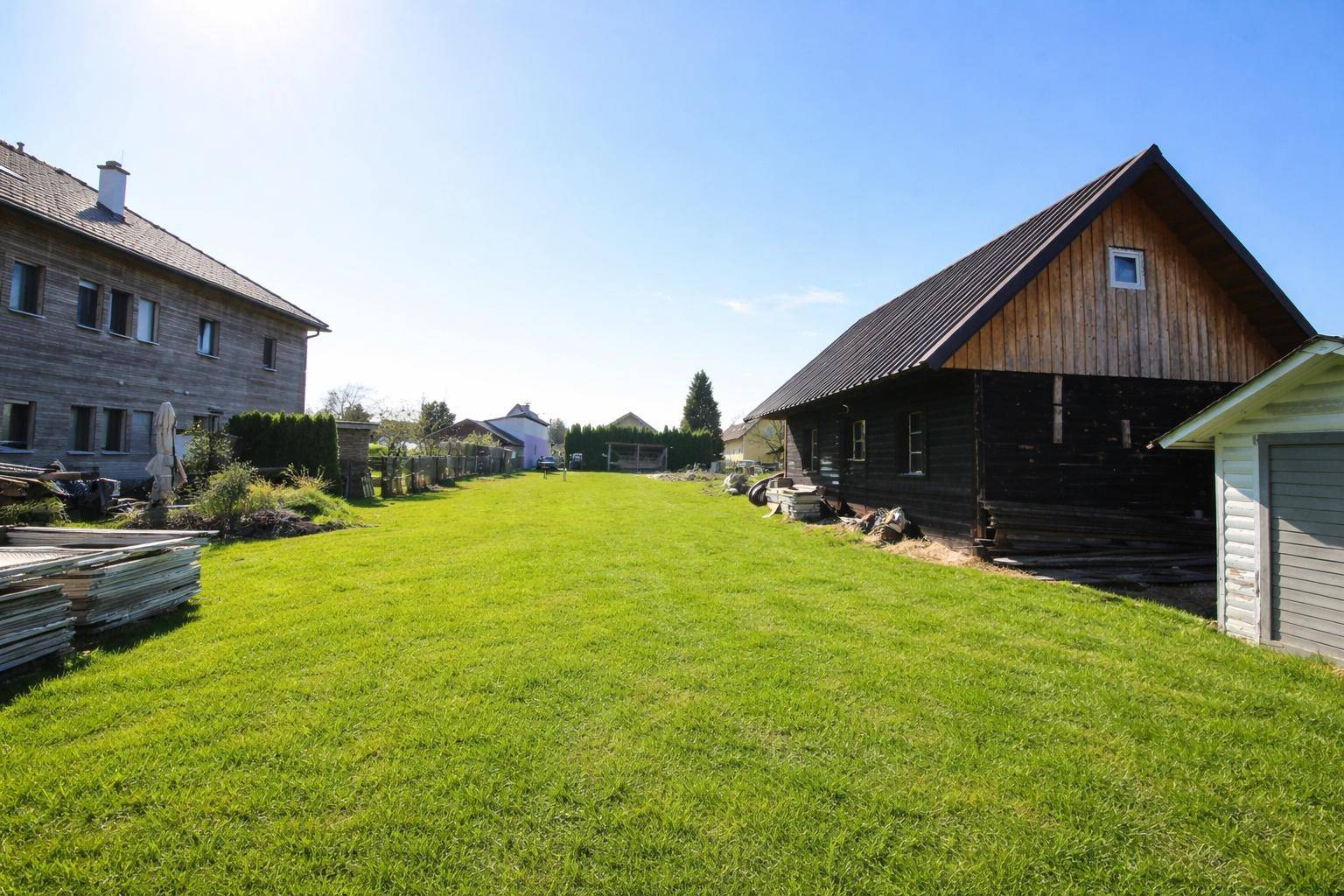 Weitläufiger Gartenbereich mit Rasenfläche zwischen dem Haupthaus und einem Nebengebäude aus Holz.