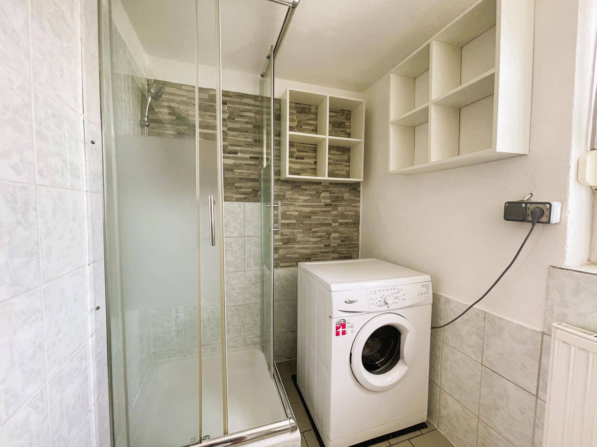 Modernes Badezimmer mit Duschkabine, Waschmaschine und praktischen Wandregalen.