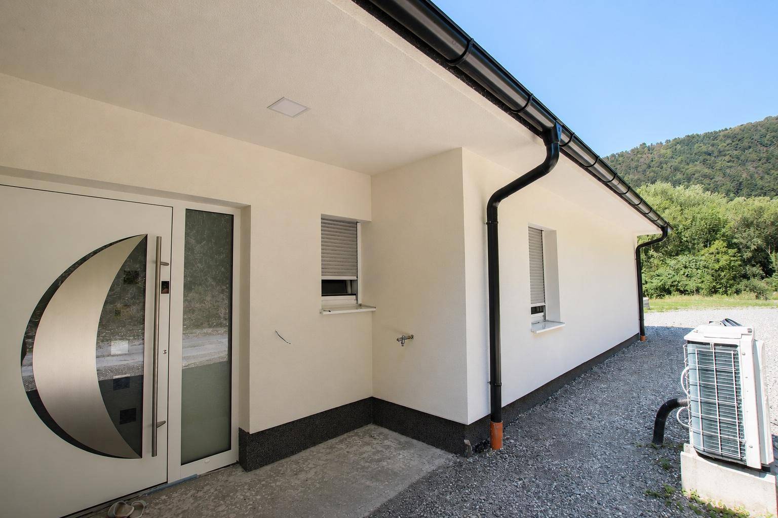 Eingangsbereich des Hauses mit moderner Tür und einer außen installierten Wärmepumpe.