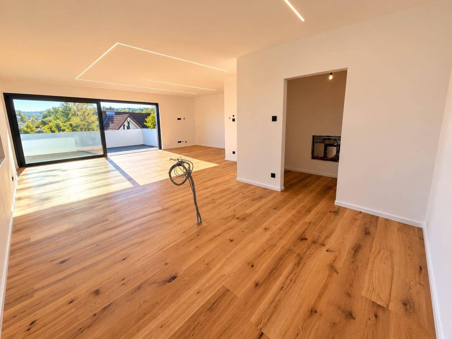 Offener Wohnbereich mit Holzboden, Terrassenzugang und einer vorbereiteten Nische für einen Kamin.