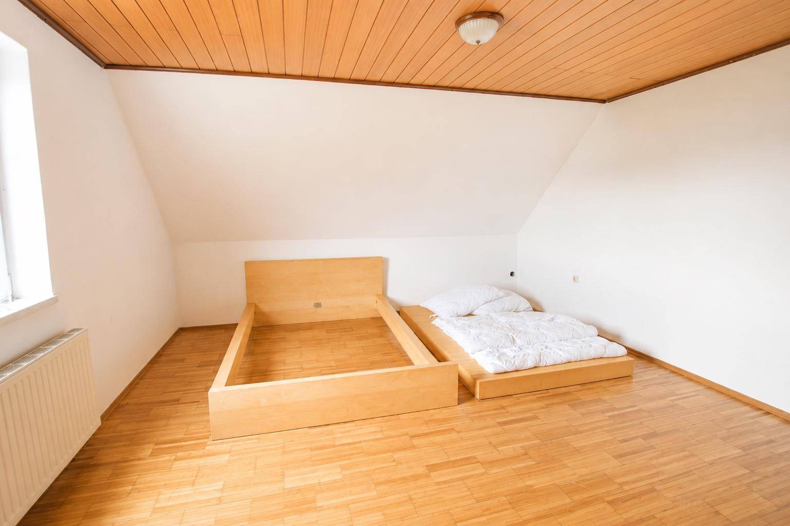 Schlafzimmer im Dachgeschoss mit Holzboden, Holzdecke und zwei Bettrahmen, hell und geräumig.