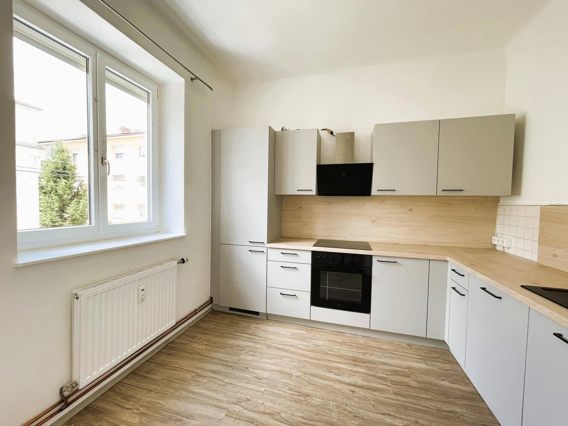 Moderne Küche mit hellgrauen Schränken, Holzarbeitsplatte und Fenster, bietet viel Tageslicht.