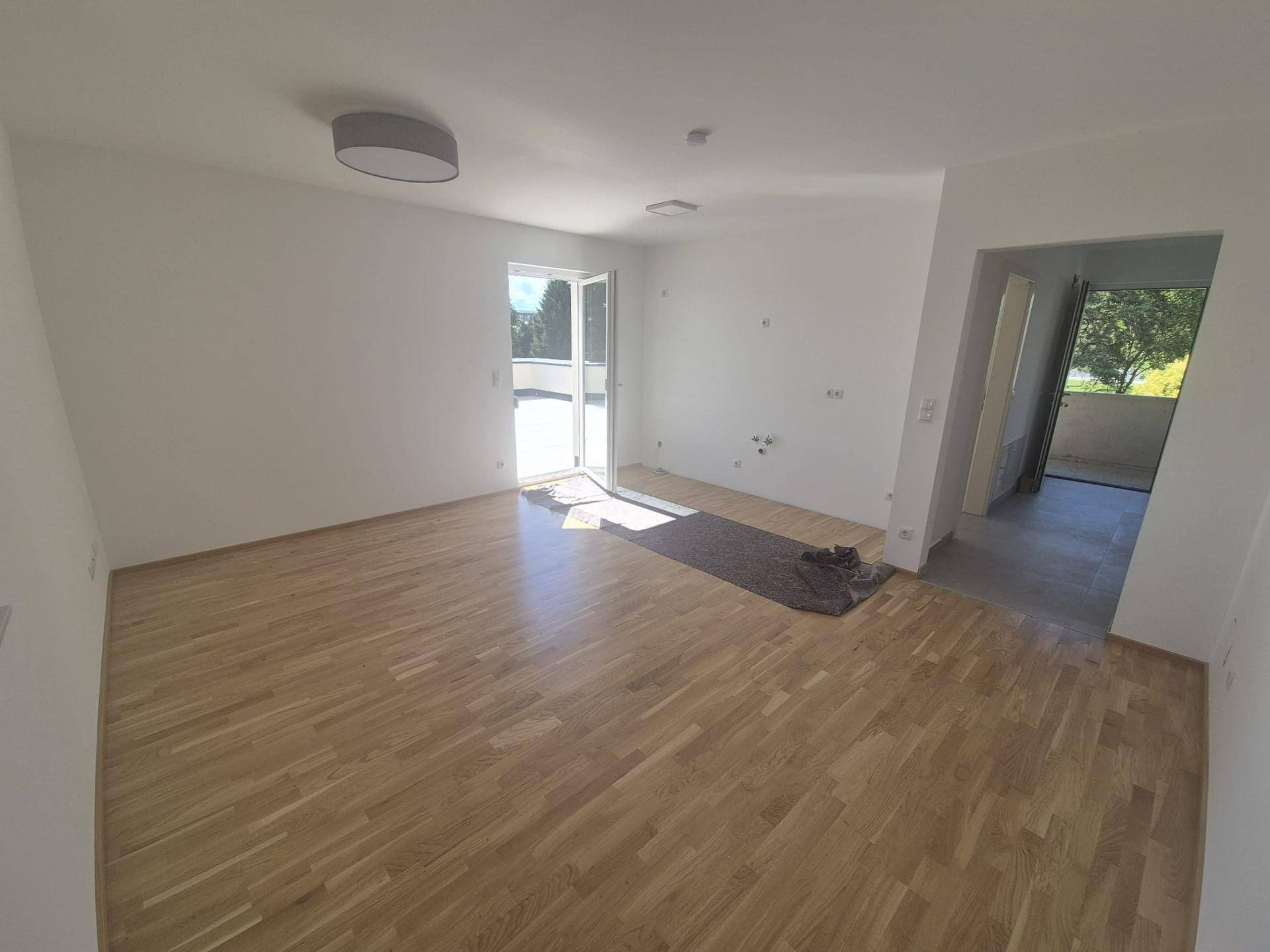Geräumiges Wohnzimmer mit hellem Parkettboden und Zugang zu einer Terrasse oder einem Balkon.