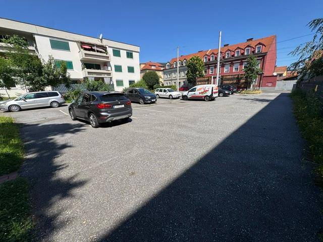 Großer Parkplatz mit verschiedenen Gebäuden im Hintergrund unter einem klaren blauen Himmel.