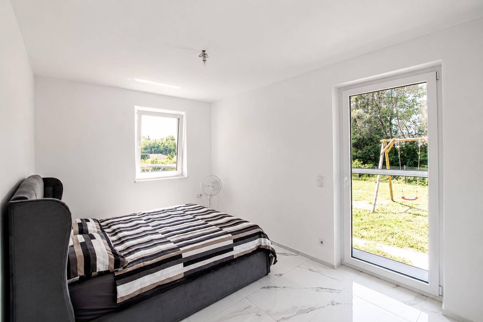 Helles Schlafzimmer mit gestreifter Bettwäsche und direktem Zugang zum Garten.