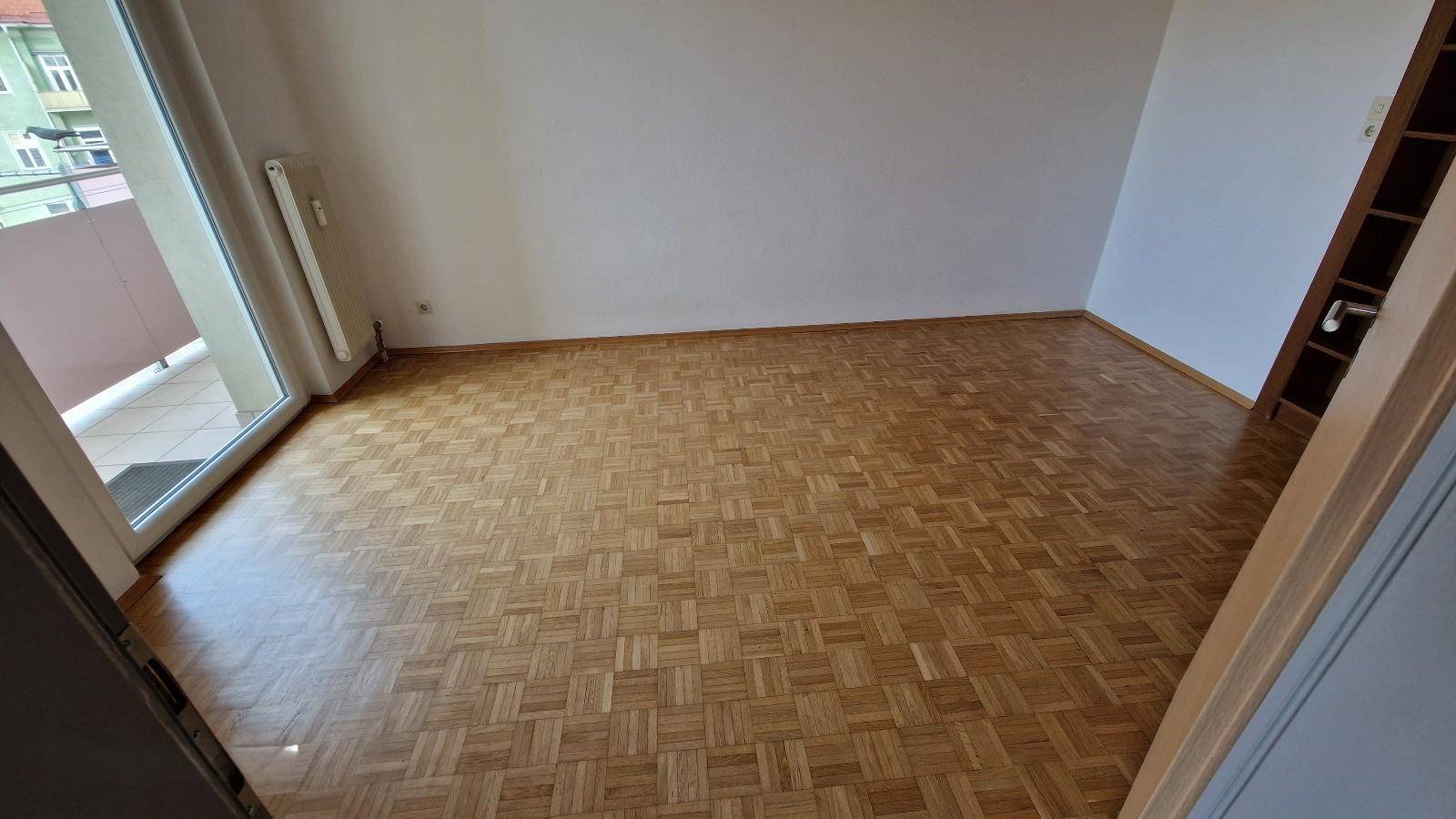 Geräumiges Zimmer mit Parkettboden und Zugang zu einem Balkon, ideal für Wohnzwecke.