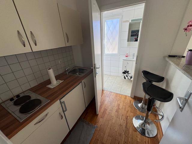 Kompakte Küchenzeile mit Kochfeld und Spüle, daneben ein Badezimmer mit Fenster.