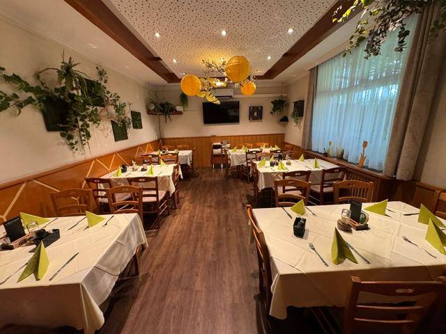 Traditioneller Speisesaal mit Holztischen, gepunkteter Decke und dekorativen Pflanzen.