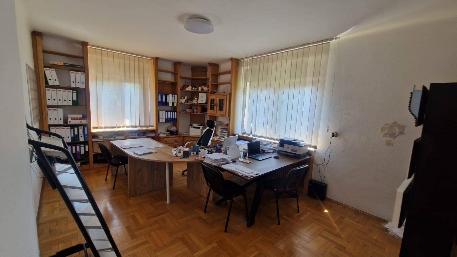 Geräumiges Büro mit Holzparkettboden, eingebauten Holzregalen und zwei Arbeitsplätzen am Fenster.