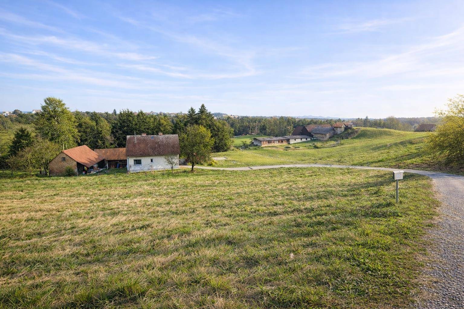 Weitläufige ländliche Landschaft mit Feldern, Bäumen und traditionellen Bauernhäusern unter blauem Himmel.