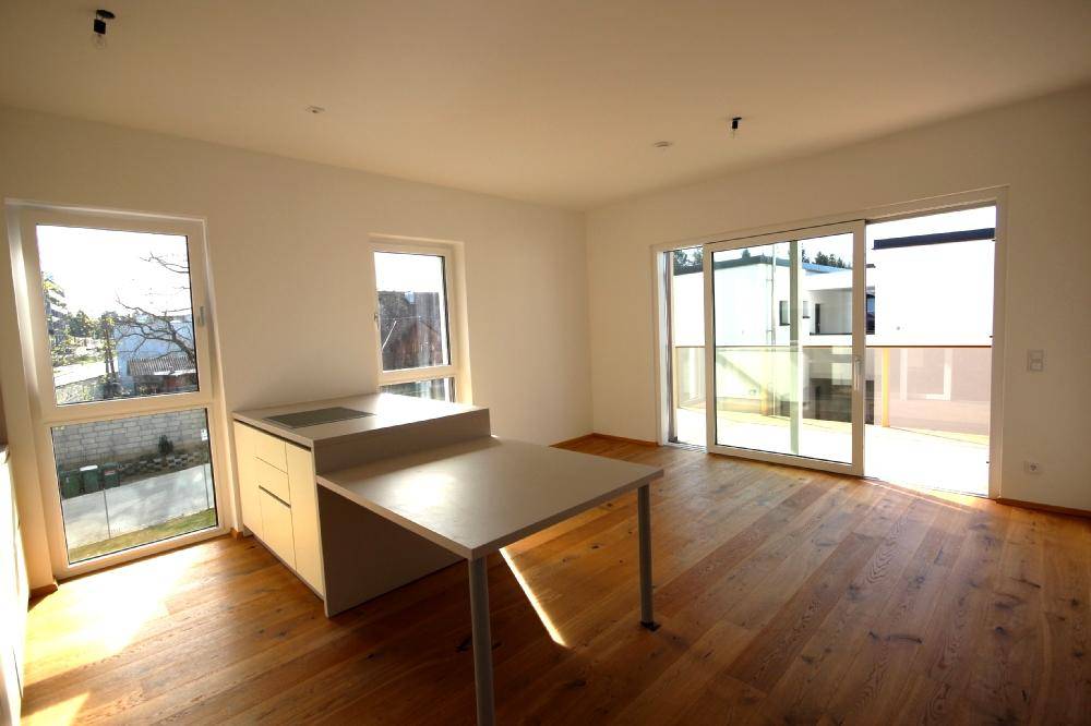 Helle, offene Küche mit Holzboden und Zugang zur Terrasse in einer Neubauwohnung.
