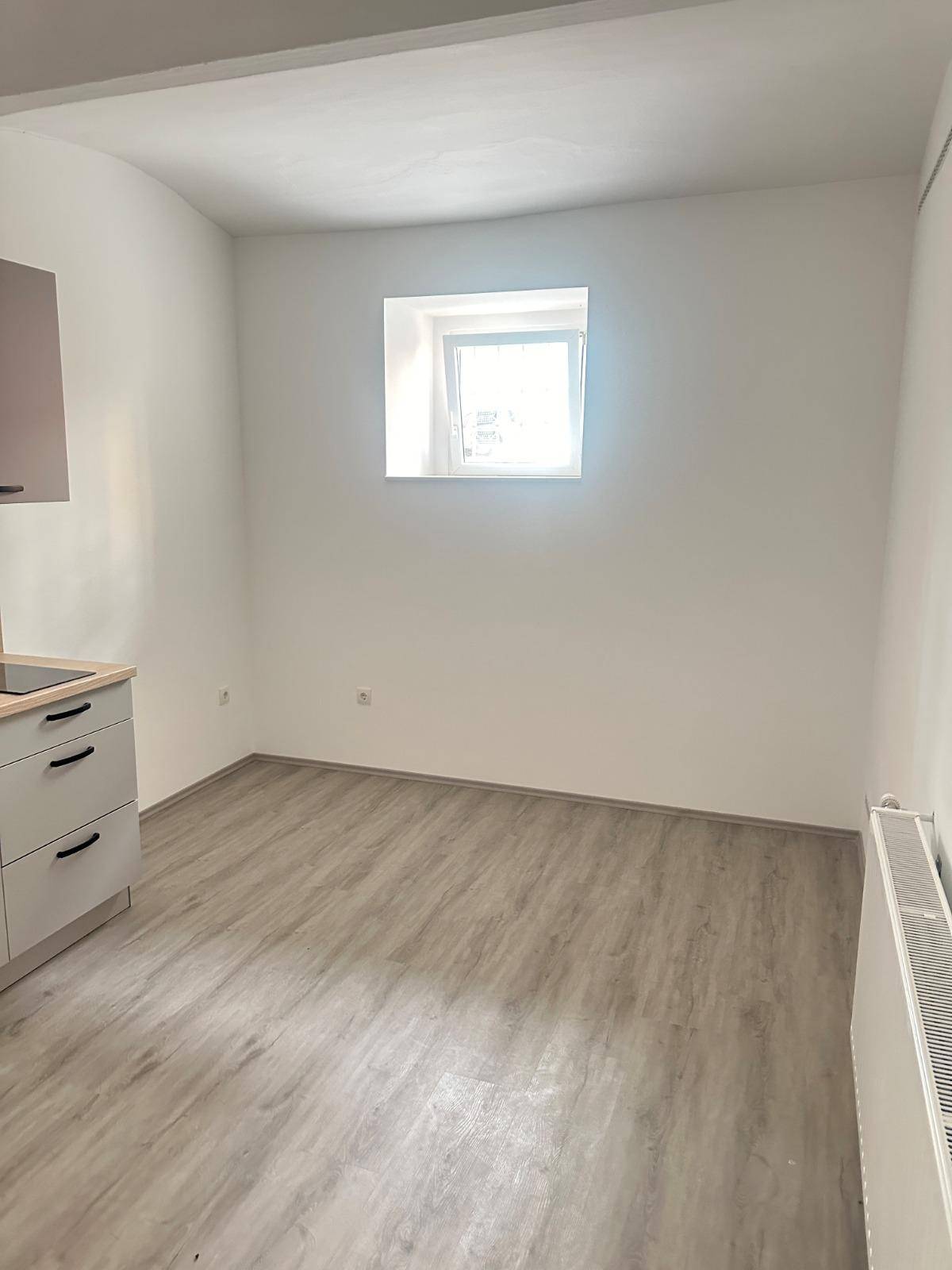 Heller Wohnraum mit Laminatboden und einem Fenster, das Tageslicht hereinlässt.