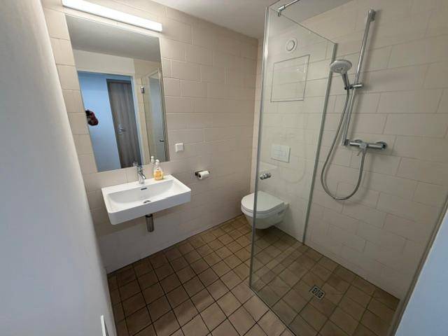 Modernes Badezimmer mit begehbarer Dusche, wandhängendem WC und hellem Fliesenboden.