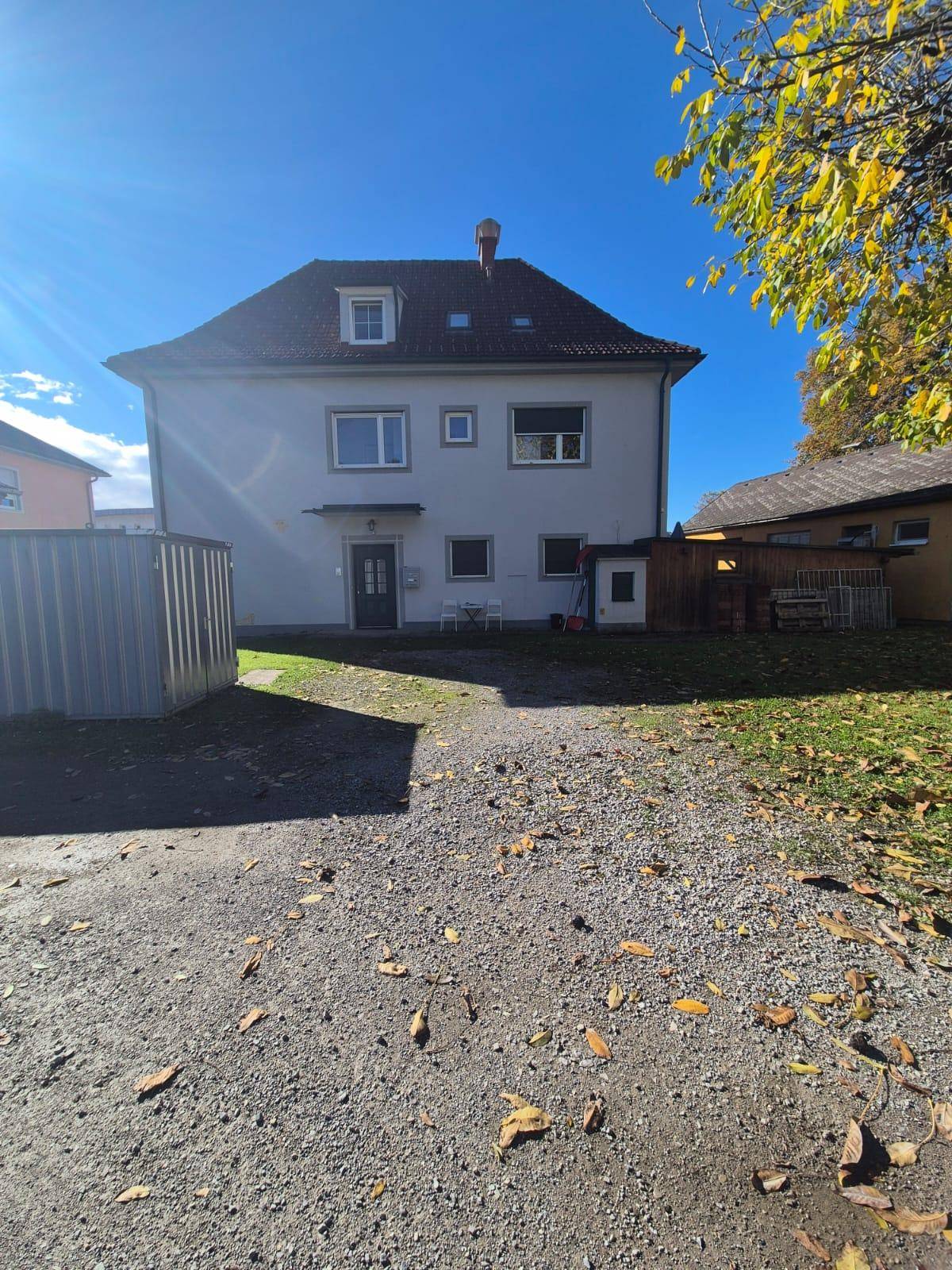 Hinterhof des Gebäudes mit Kiesfläche, Rasen und Bäumen unter blauem Himmel.