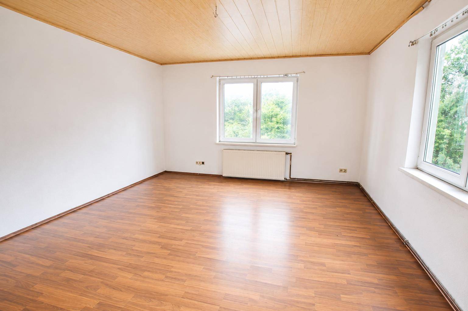 Geräumiges, helles Zimmer mit Laminatboden und Holzdecke, ideal als Wohn- oder Schlafzimmer.