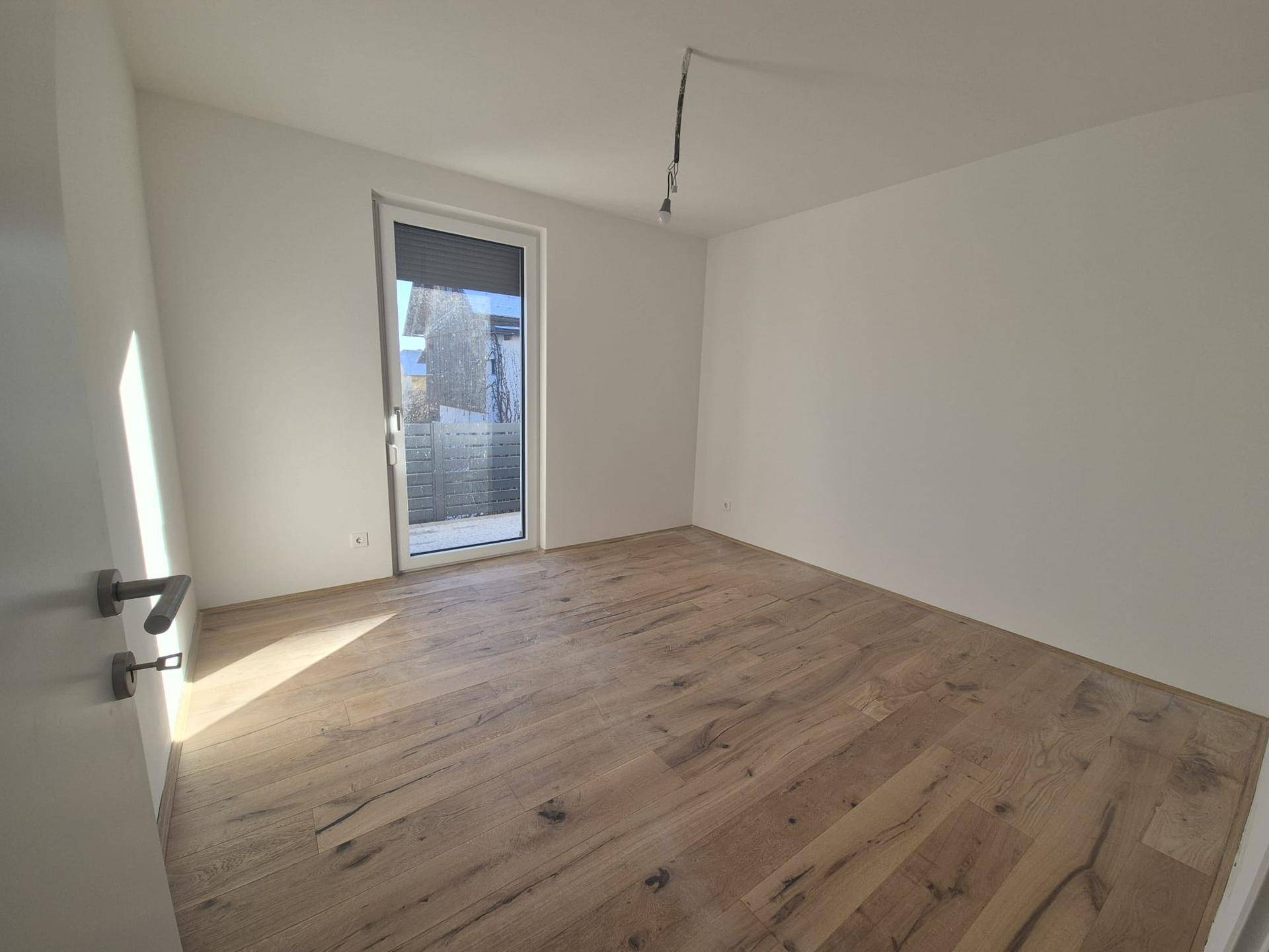 Lichtdurchflutetes Zimmer mit modernem Holzboden und großem Fenster, bereit zum Einzug.