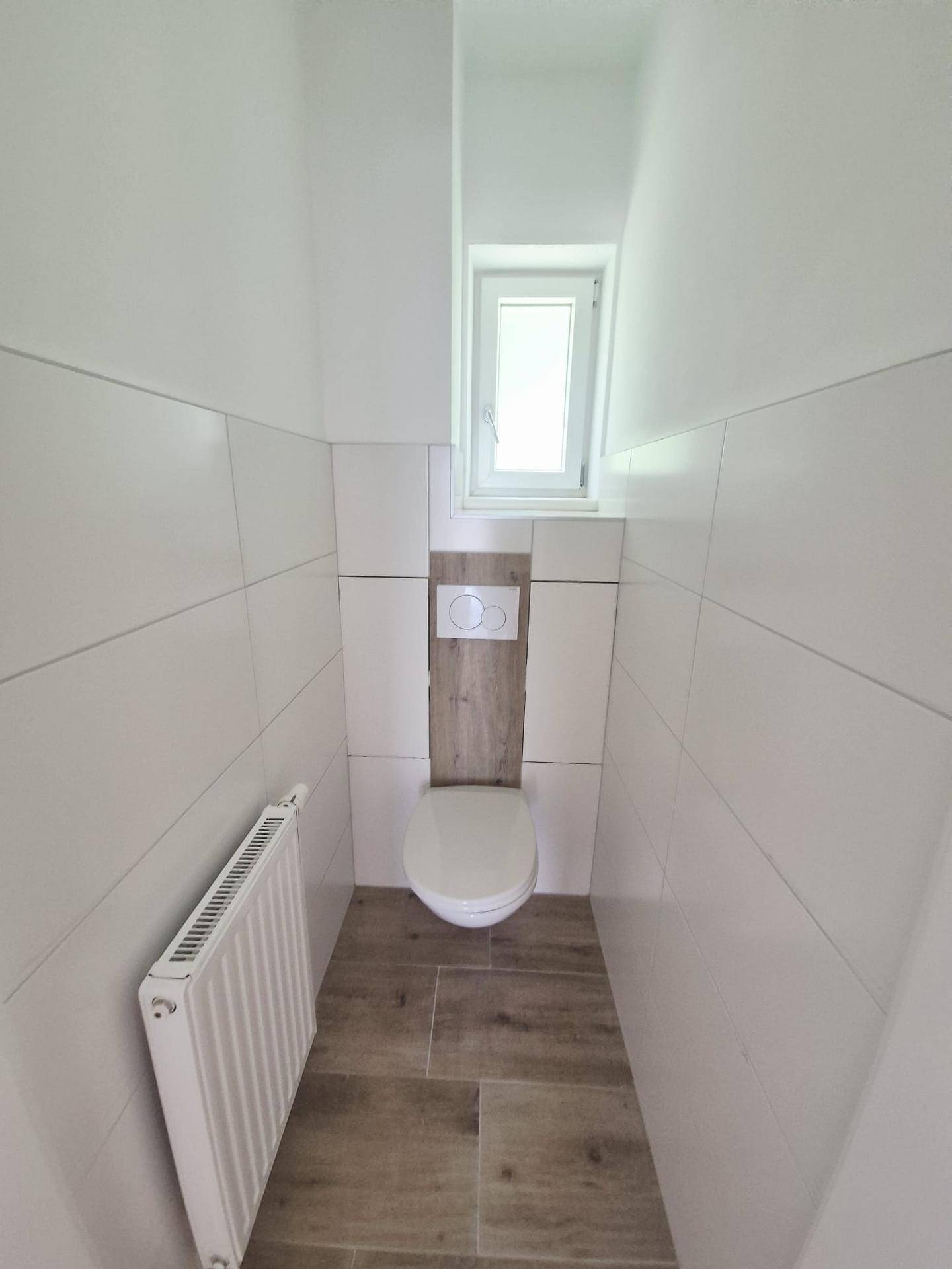 Separates WC mit wandhängender Toilette, kleinem Fenster und modernem Fliesenboden.