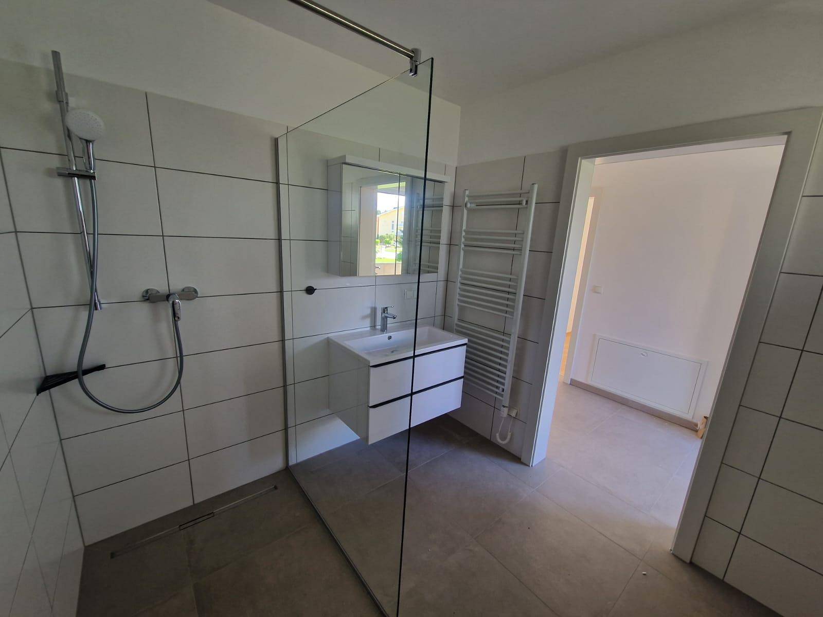 Helles Badezimmer mit moderner Ausstattung, ebenerdiger Dusche und beheiztem Handtuchhalter.