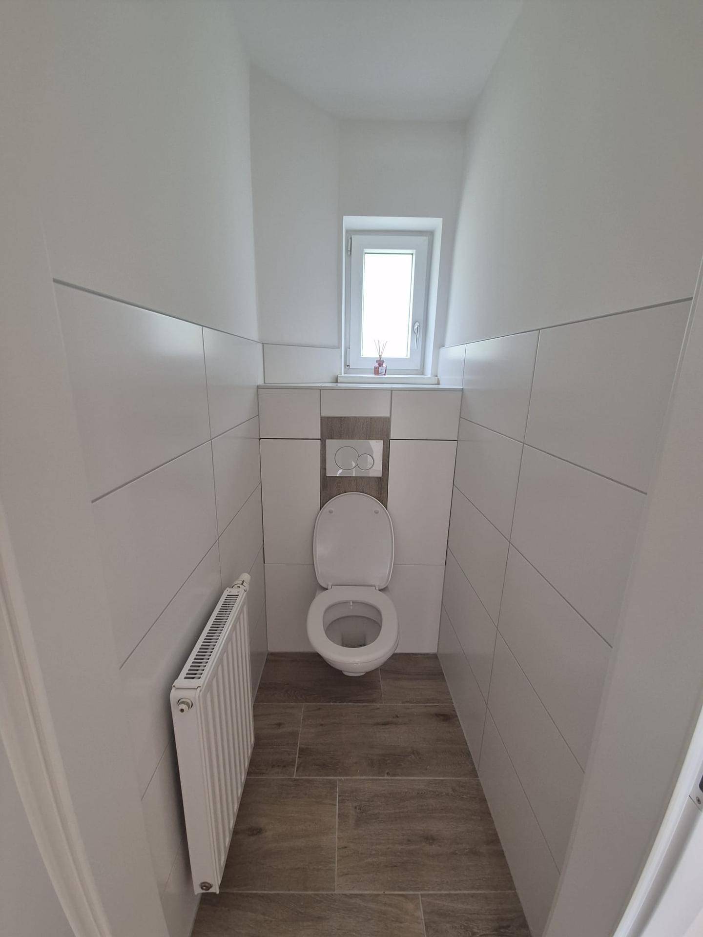 Separates Gäste-WC mit wandhängender Toilette, kleinem Fenster und modernen Fliesen.