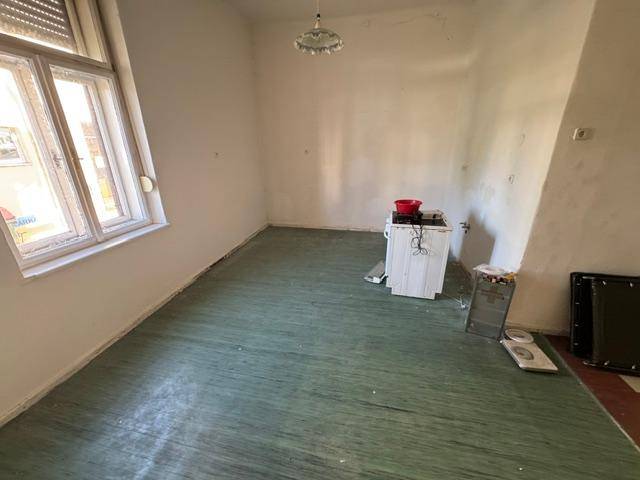 Kleiner Raum mit grün gestrichenem Dielenboden und Fenster, renovierungsbedürftig.