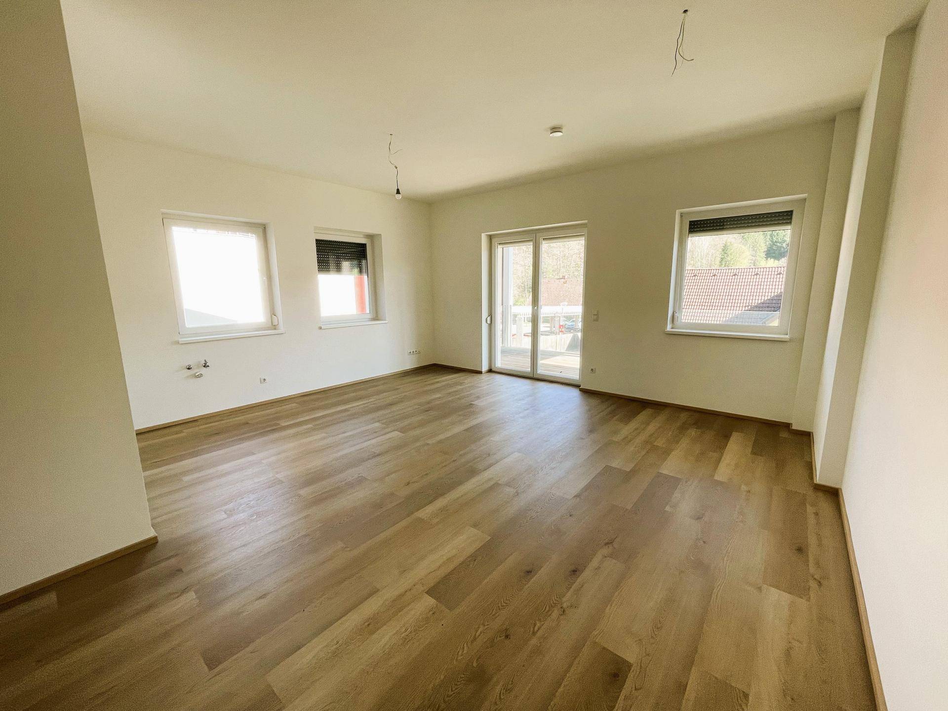 Geräumiges Wohnzimmer mit Laminatboden und Zugang zu einem Balkon.