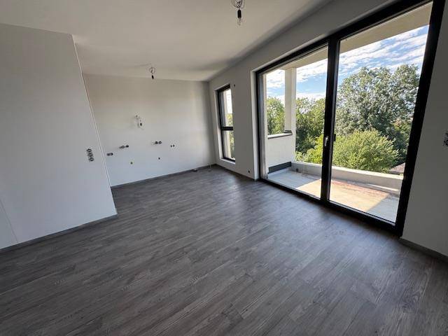 Unfertiges Zimmer mit Laminatboden, großen Fenstern und Zugang zu einem Balkon.